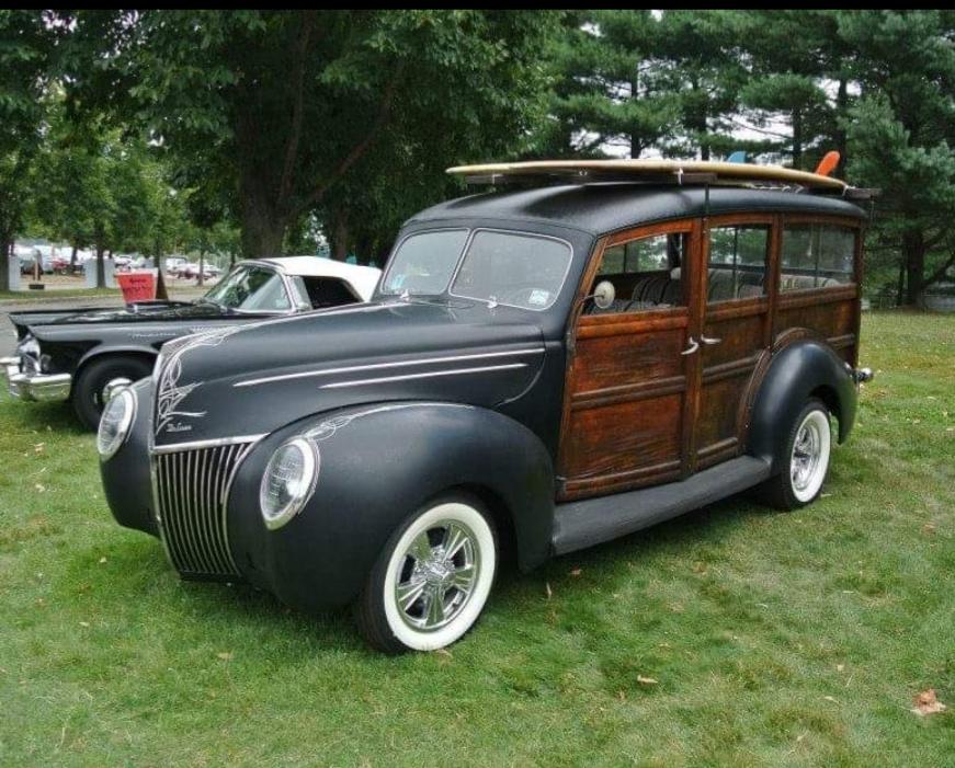 Black 1939 Ford woodie wagon with a surfboard on the roof